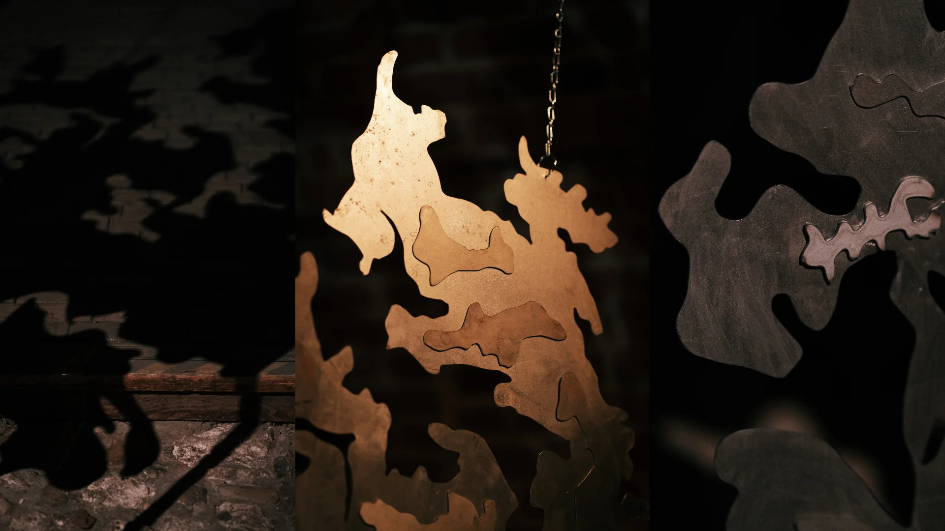Suspended pale metal sculpture with complex organic contours illuminated against a dark gallery background.