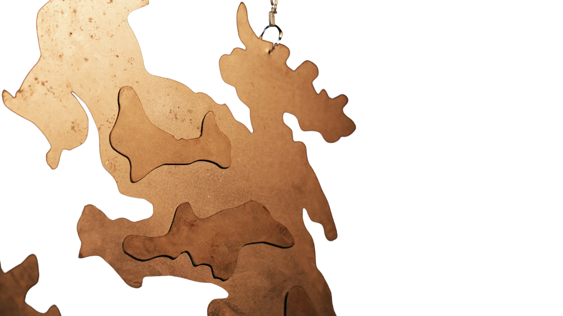 Close-up of a warm-toned metal sculpture with rounded organic extensions and irregular cut-out shapes.
