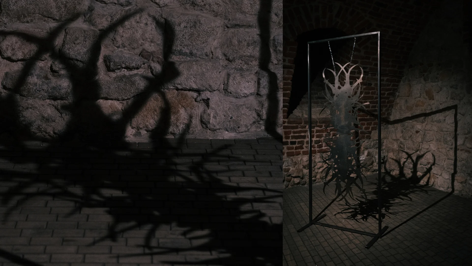 Branching abstract metal sculpture displayed against weathered stone and brick walls.