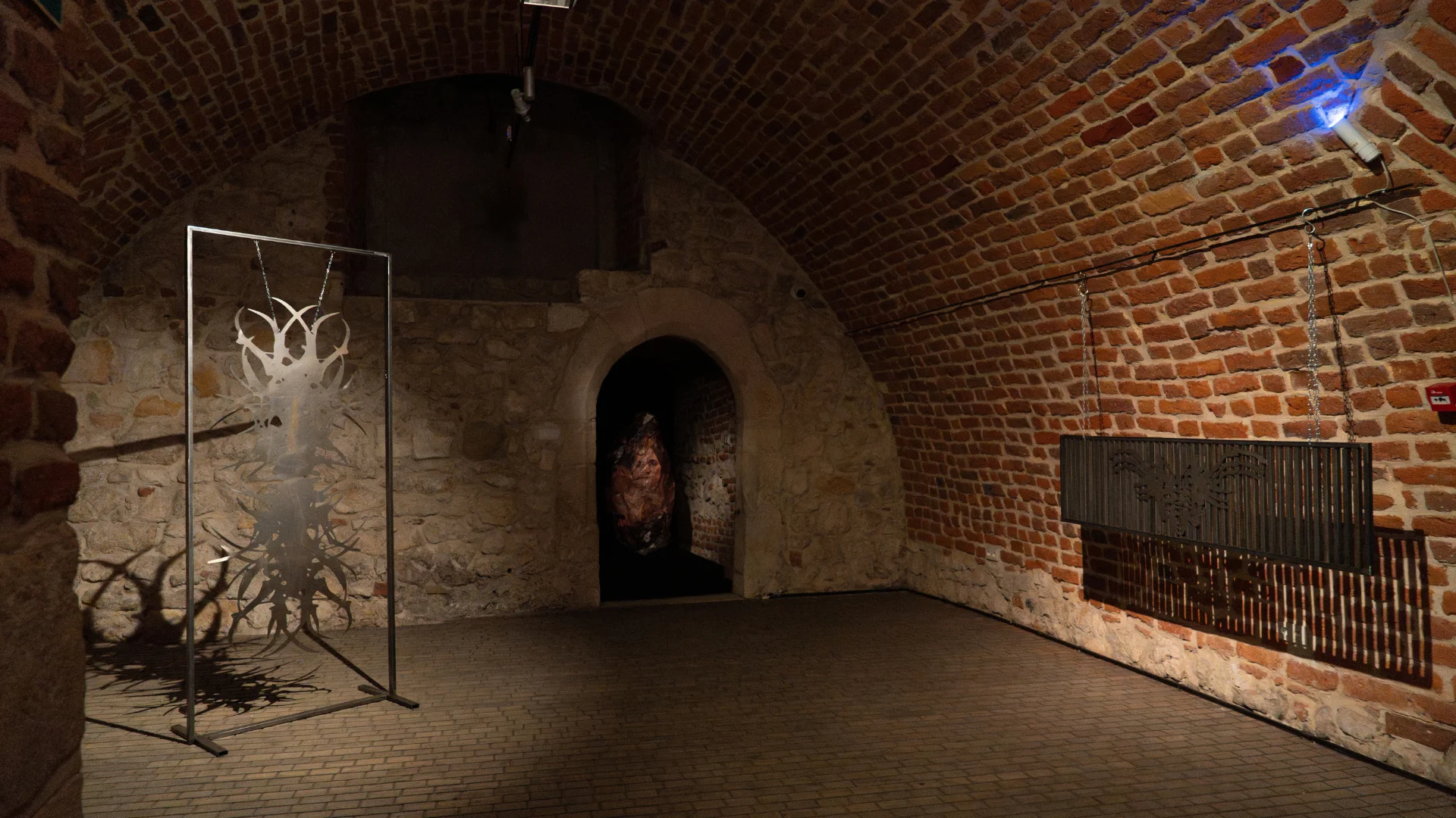 Historic brick gallery with vaulted ceiling and sculptural artworks displayed throughout the space.