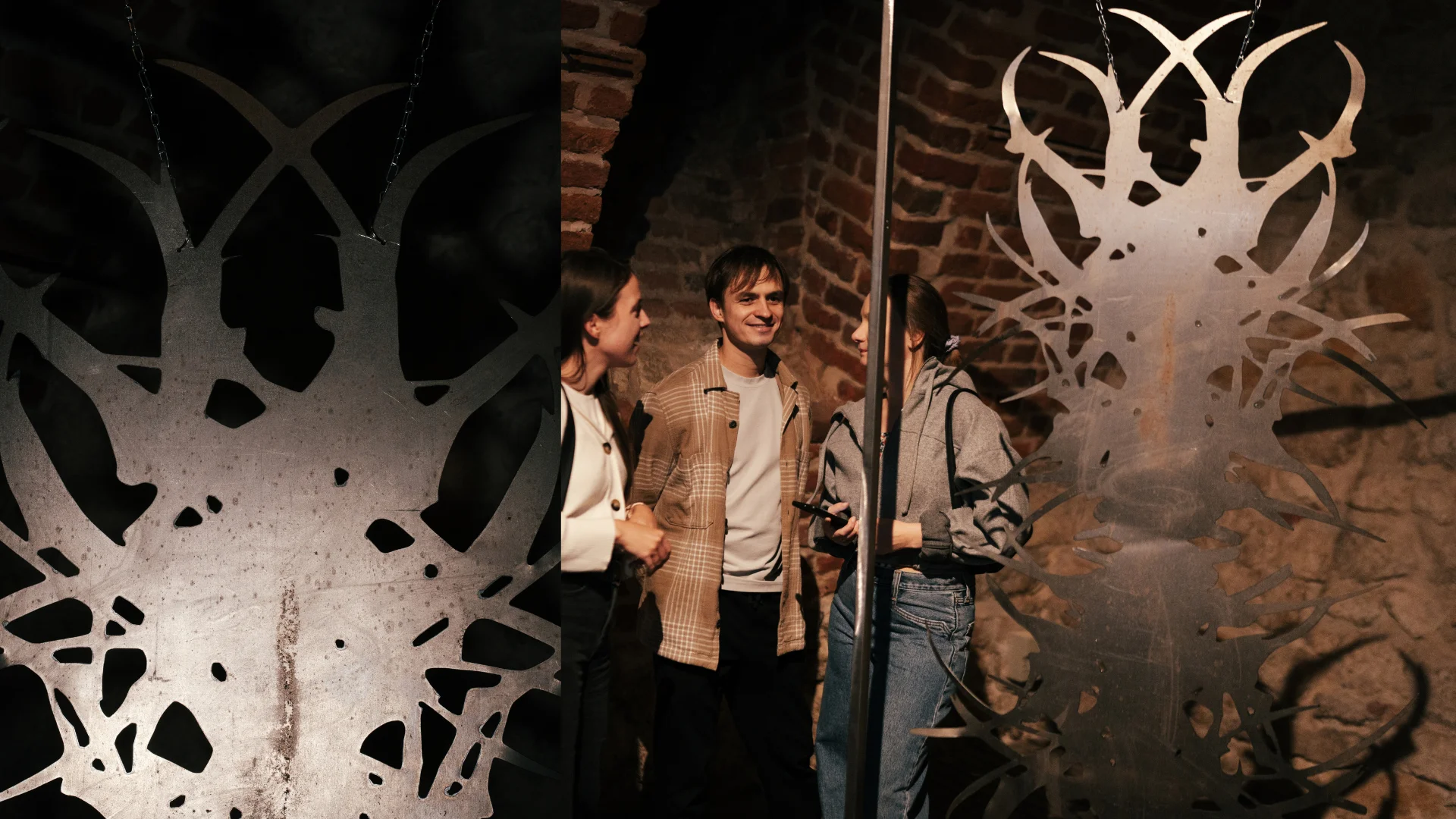 Visitors standing beside a suspended abstract sculpture in a historic brick exhibition space.