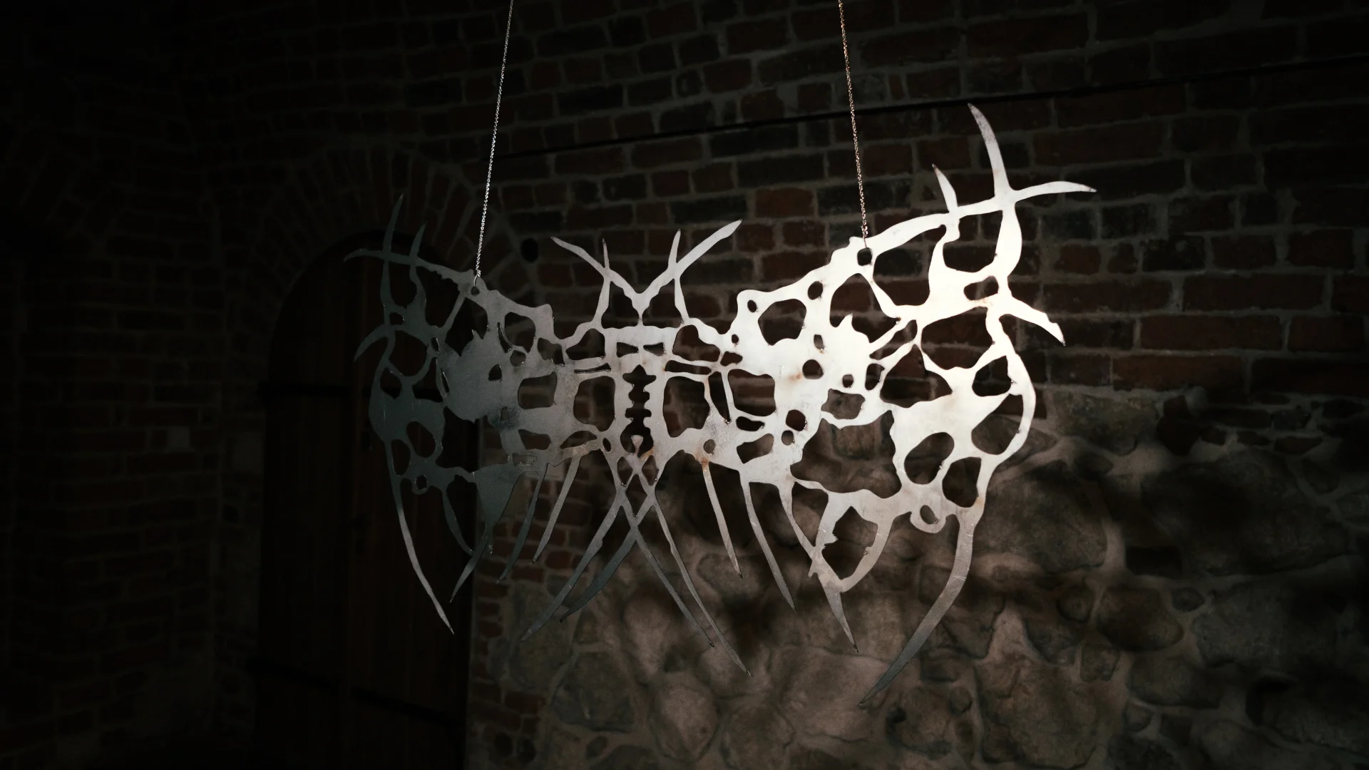 Intricate branching metal sculpture illuminated against the brick walls of an exhibition space.