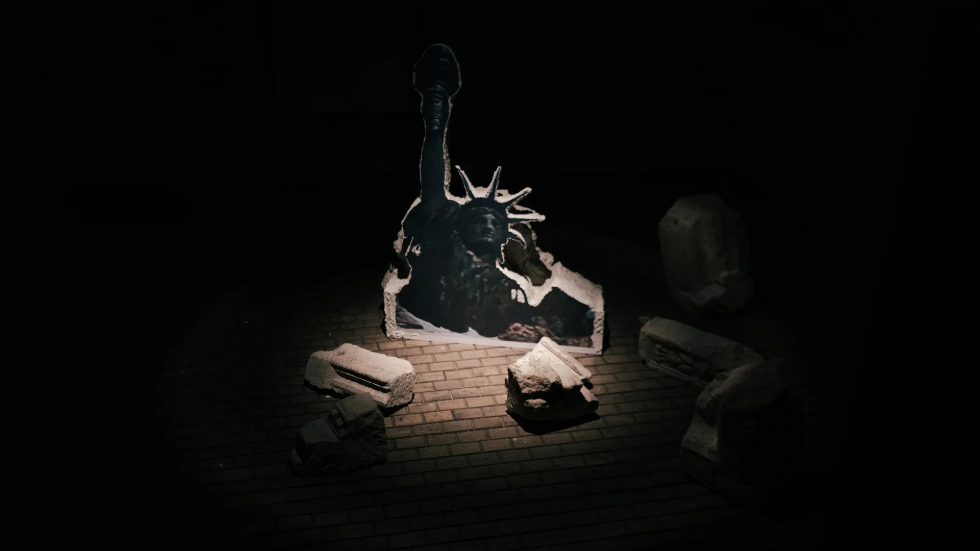 Fragmented Statue of Liberty installation illuminated dramatically in a dark exhibition space.