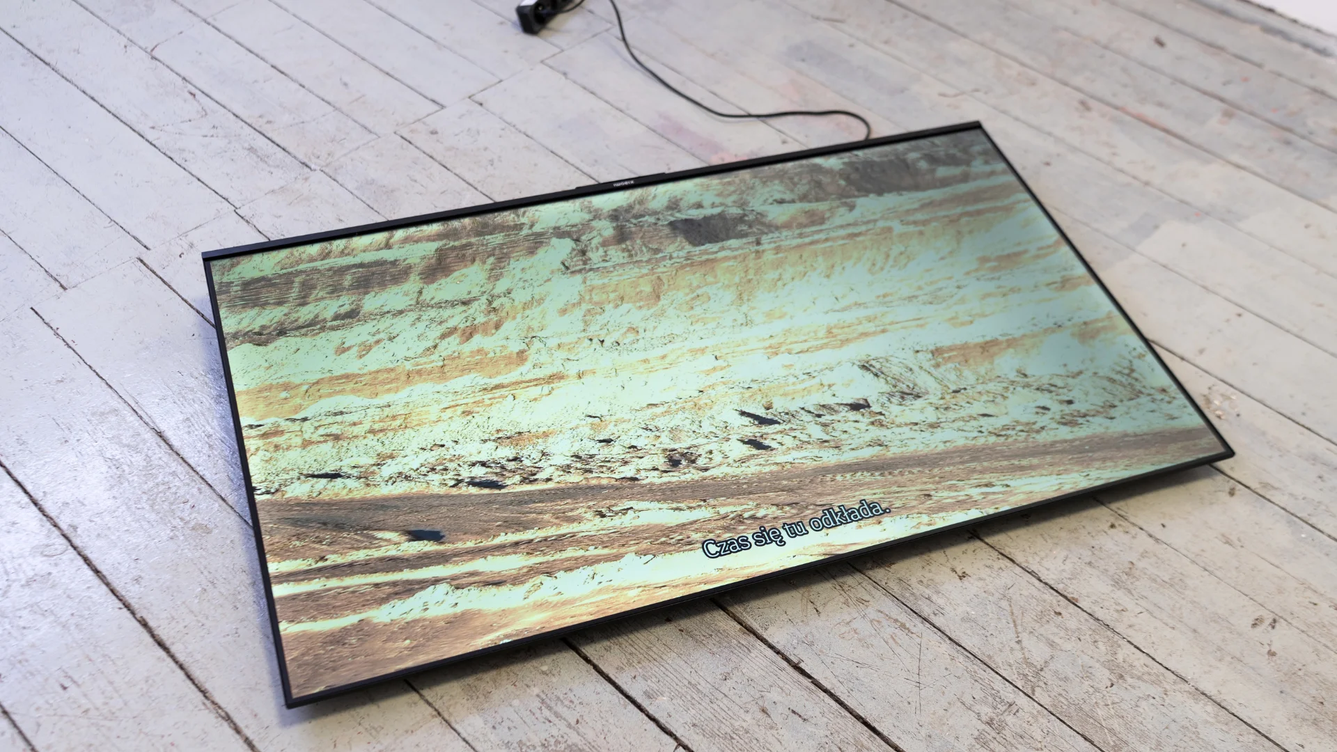 Flat television screen on a pale wooden floor displaying a terraced post-mining landscape.